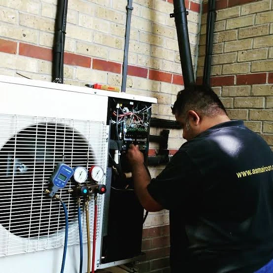 Technician inspecting a wall-mounted outdoor air-conditioning unit